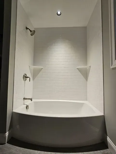 White tiled shower and tub with chrome fixtures, built-in shelves, and a recessed ceiling light by Syn-Mar
