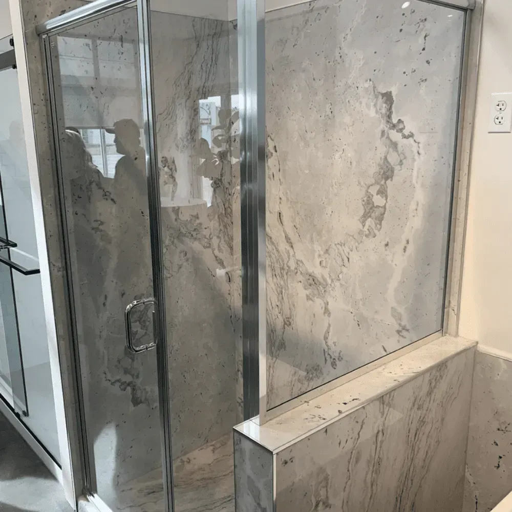 Glass shower enclosure with gray marble tile walls and a white electrical outlet by Syn-Mar