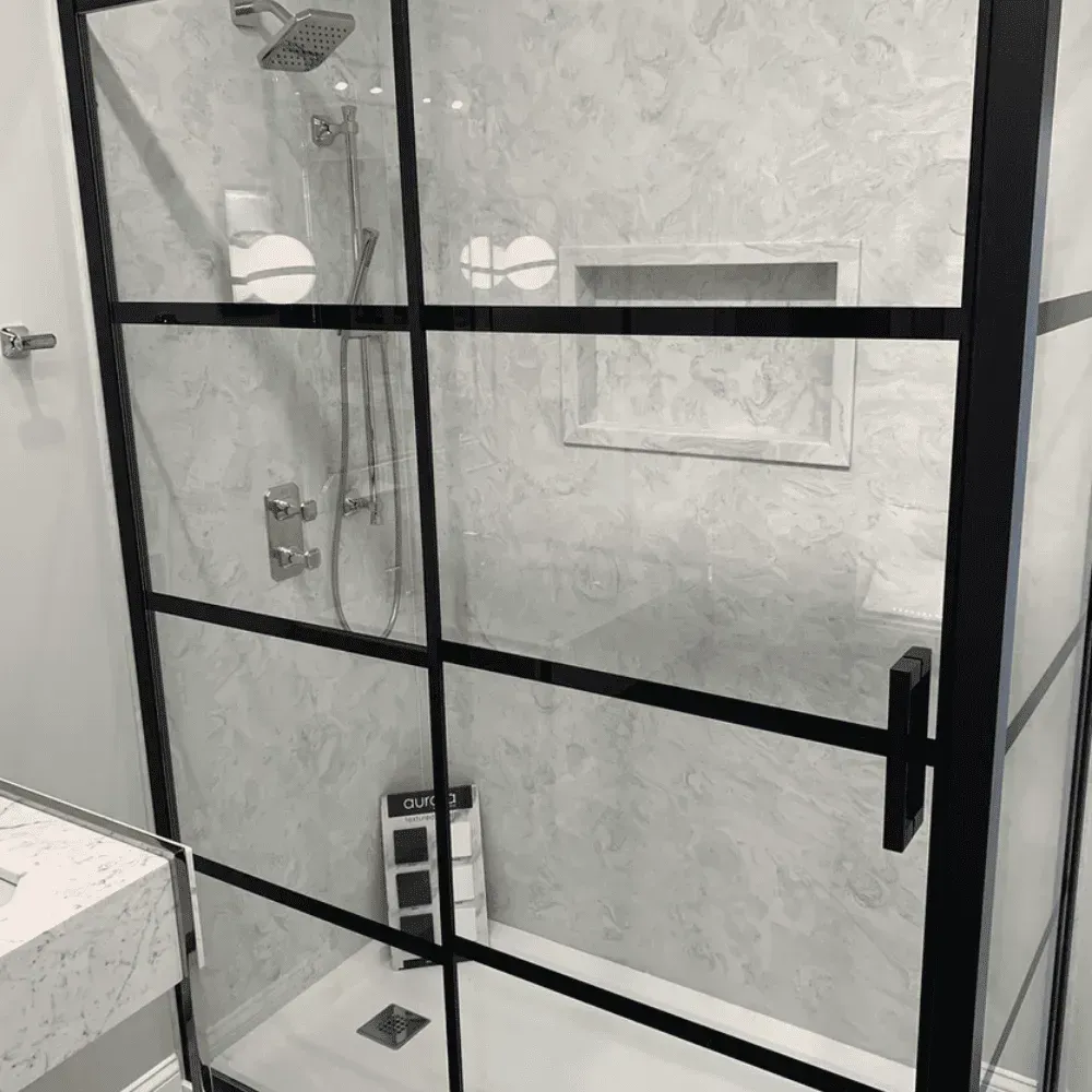 Black-framed shower with glass doors, grey marble-like tile, and a built-in shelf by Syn-Mar