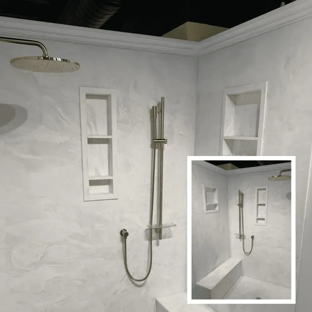 White tiled shower stall with built-in shelves, showerhead, grab bars, and a handheld sprayer.