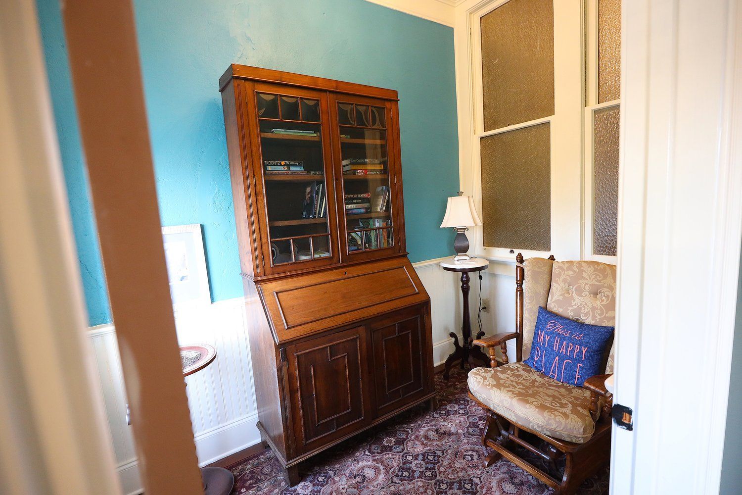 A room with a bookcase , chair , table and lamp.