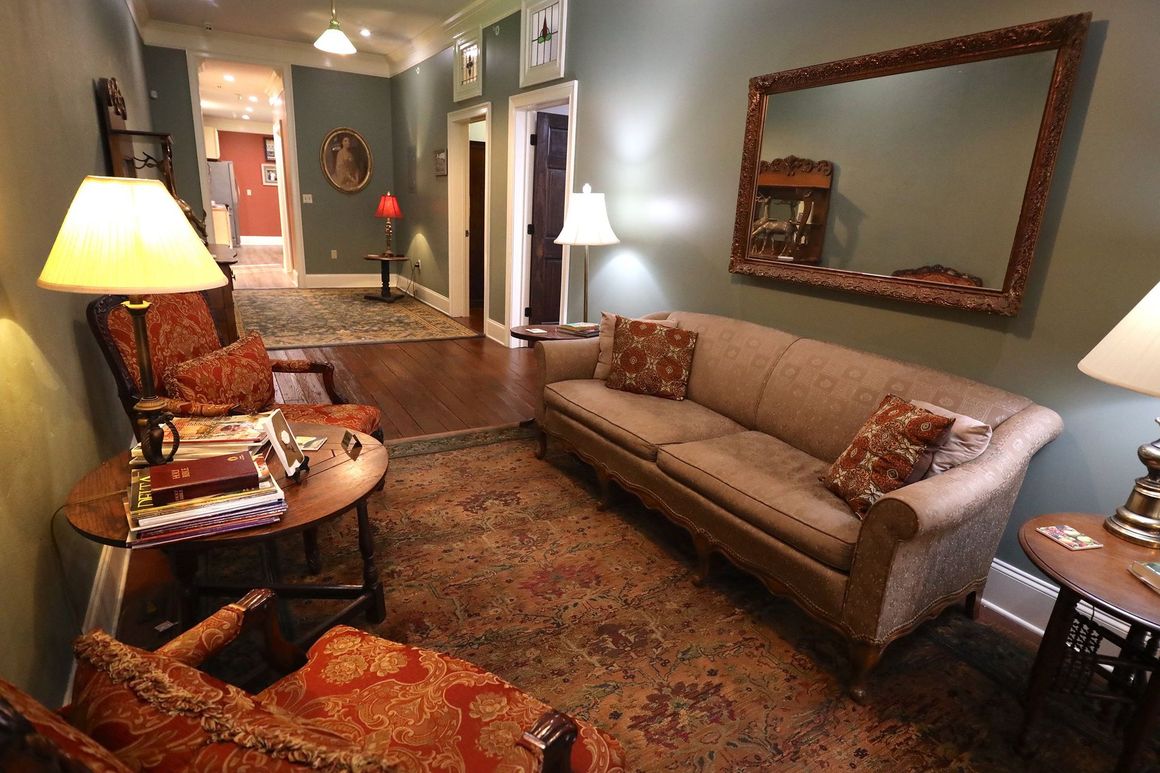A living room with a couch , chairs , lamps and a mirror