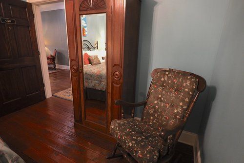 A bedroom with a rocking chair and a wardrobe with a mirror.