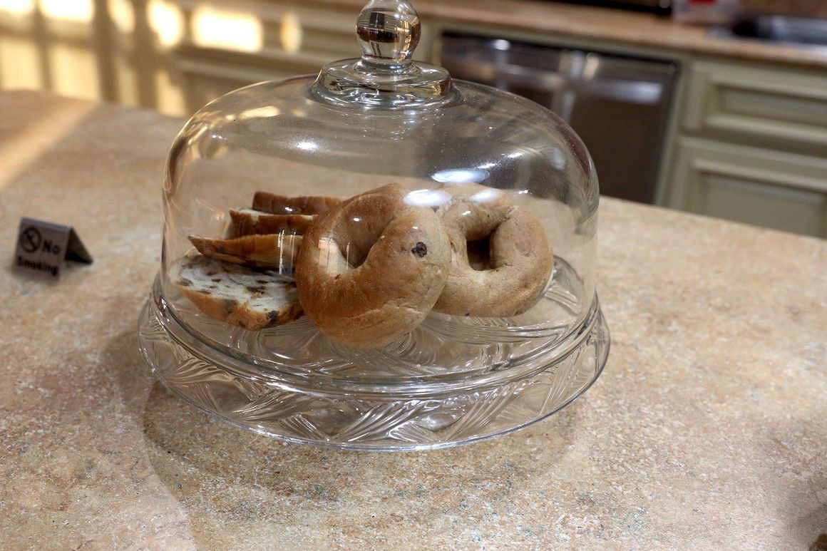 Three bagels are sitting under a glass dome on a counter.