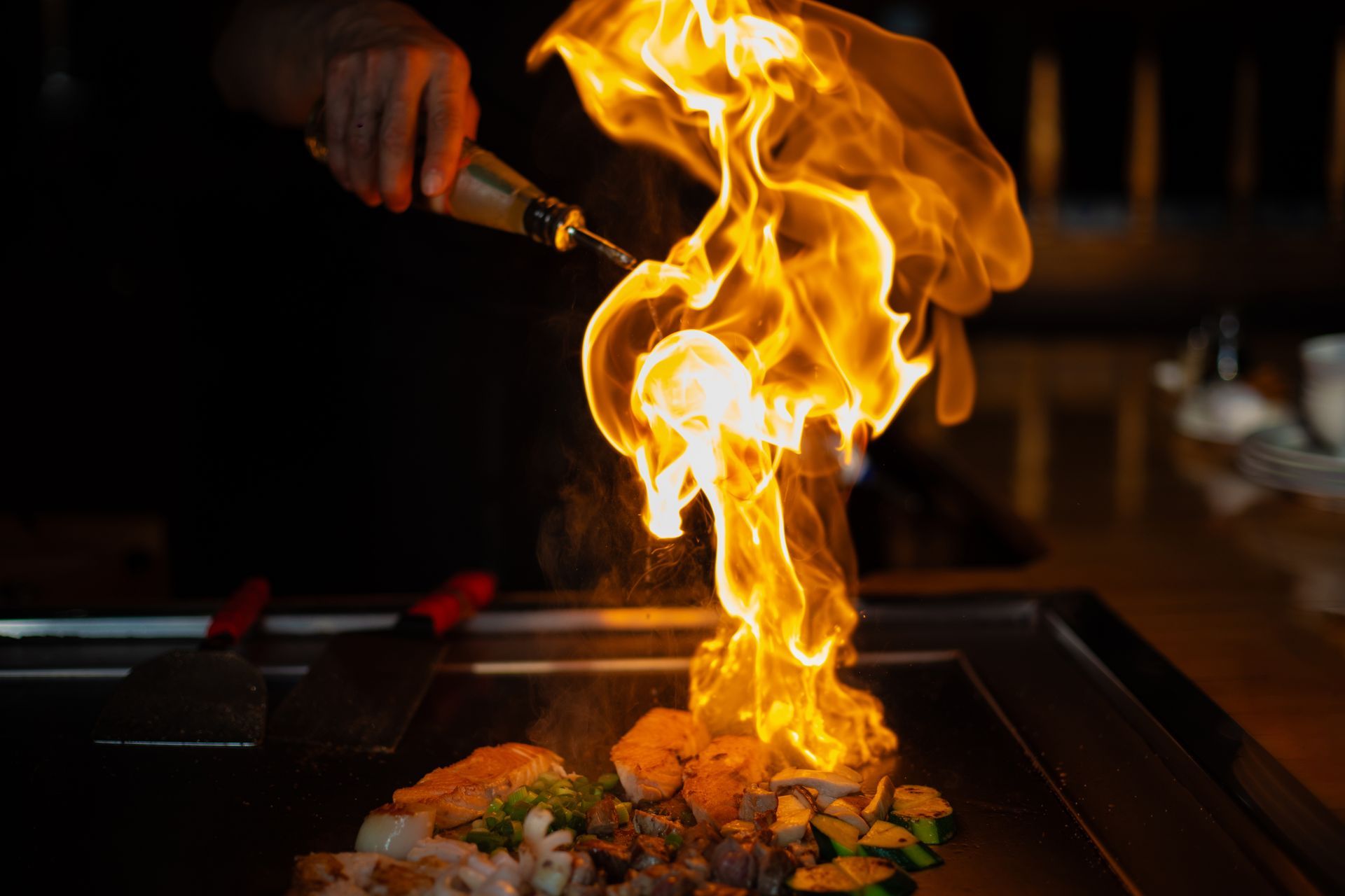 A person is cooking food on a grill with flames coming out of it.