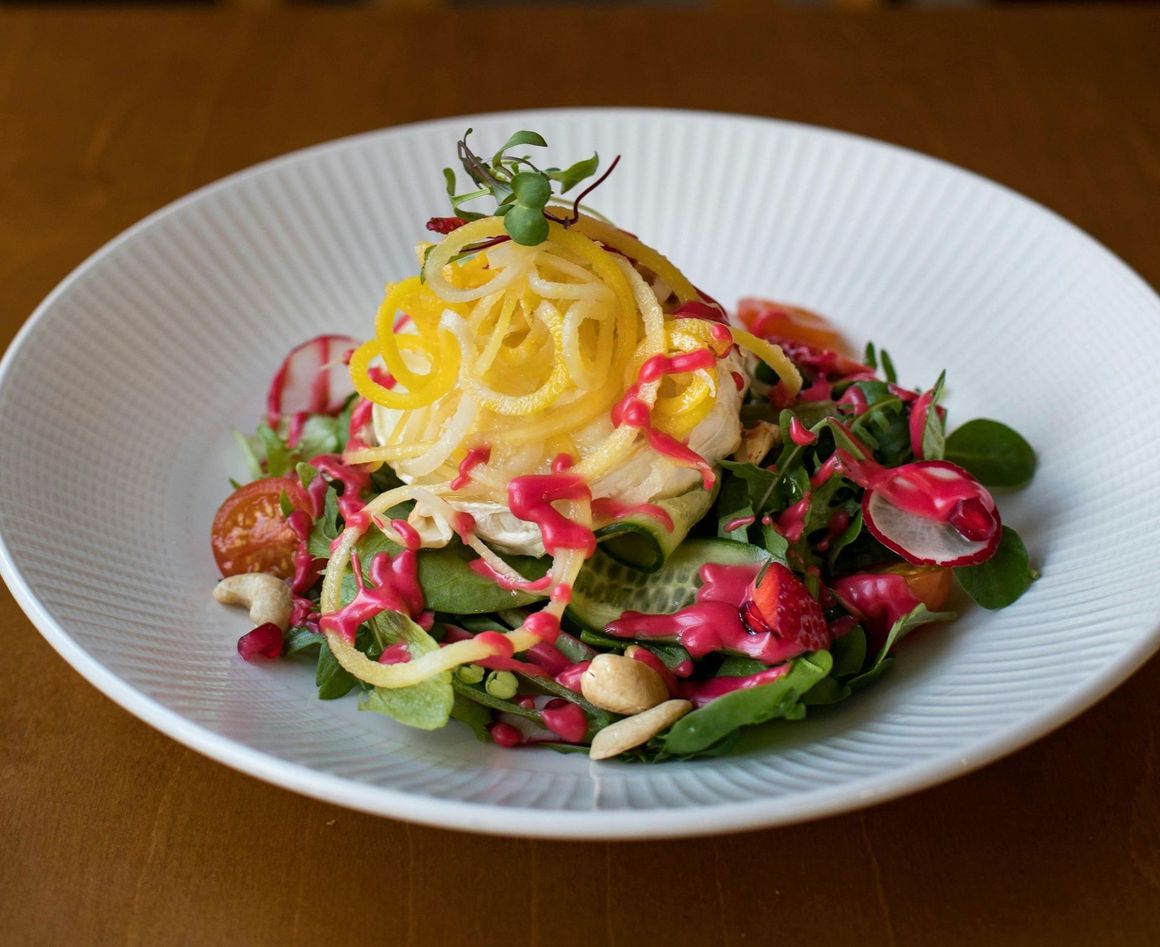 A white plate topped with a salad of noodles and vegetables on a wooden table.
