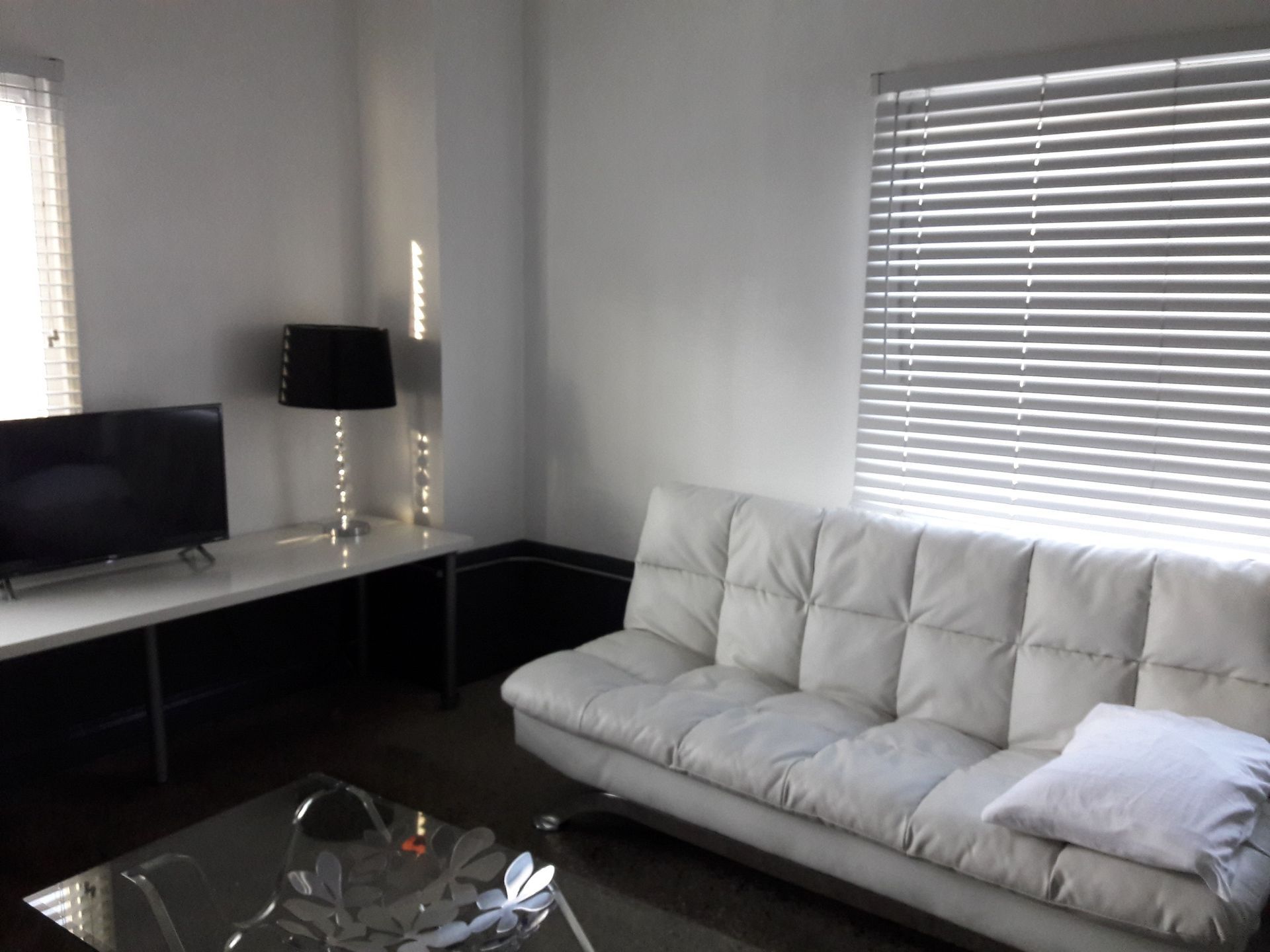 A white tufted sofa sits in a living room next to a white desk with a black lamp and a television.