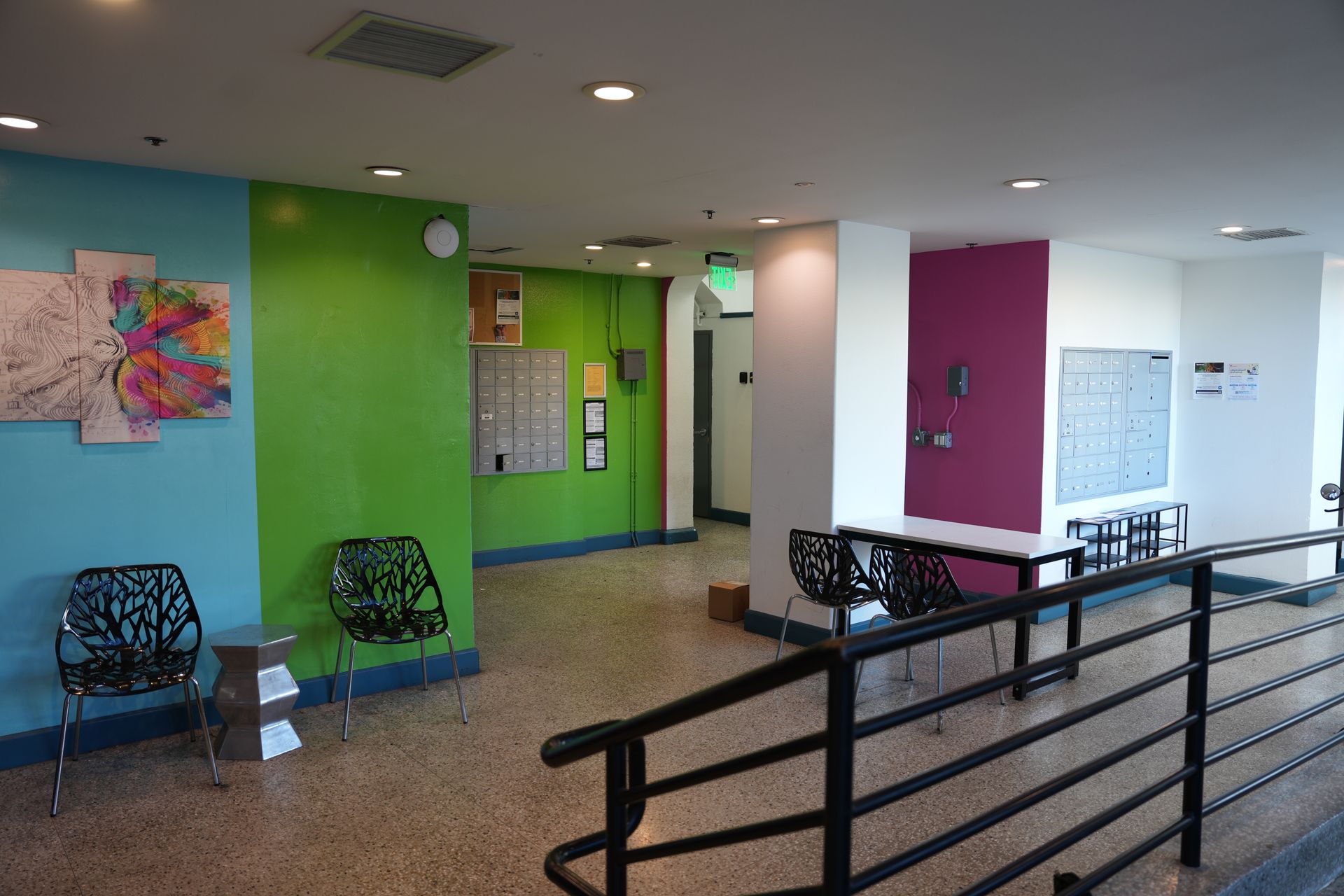 An interior lobby with colorful walls, decorative chairs, and a metal staircase railing leading to a back hallway.