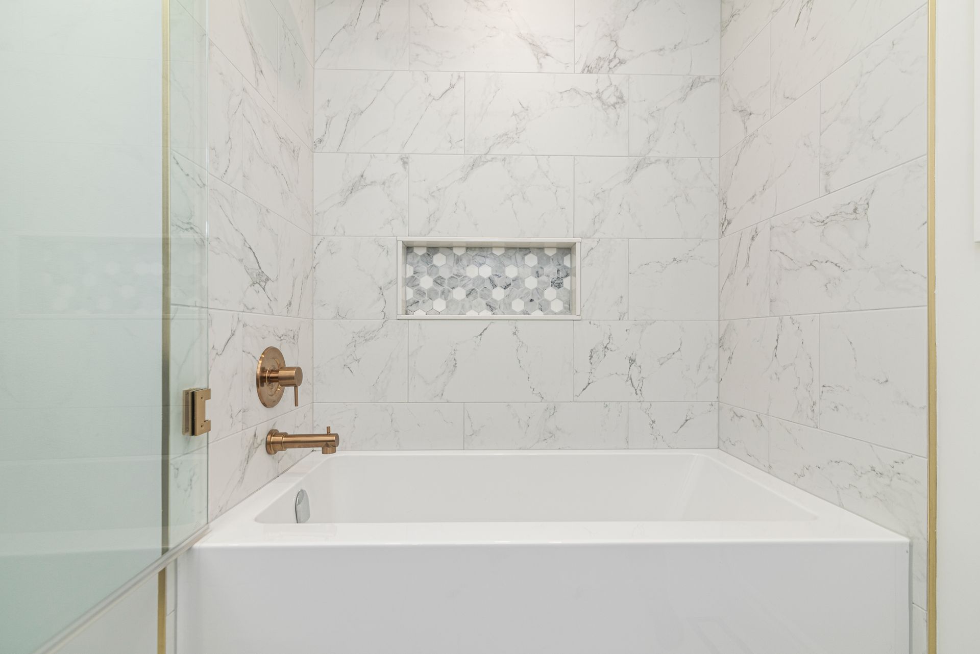a bathtub in a bathroom with marble tiles and a shower stall .