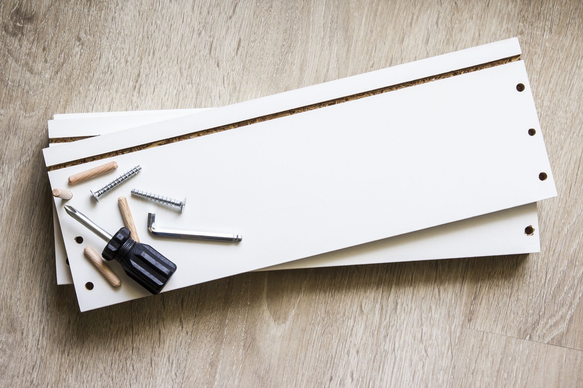 A stack of white boards with screws and a screwdriver on a table.