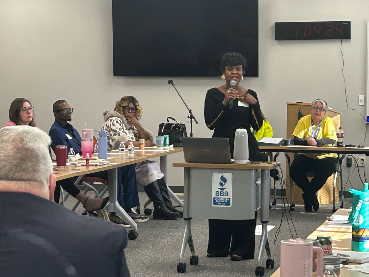 Radio studio with microphones on boom arms, a control board, and a banner.