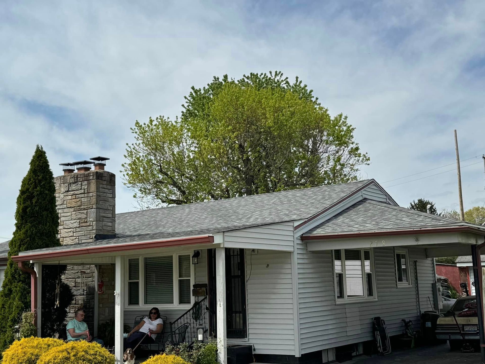 Two people are sitting on a porch of a white house.