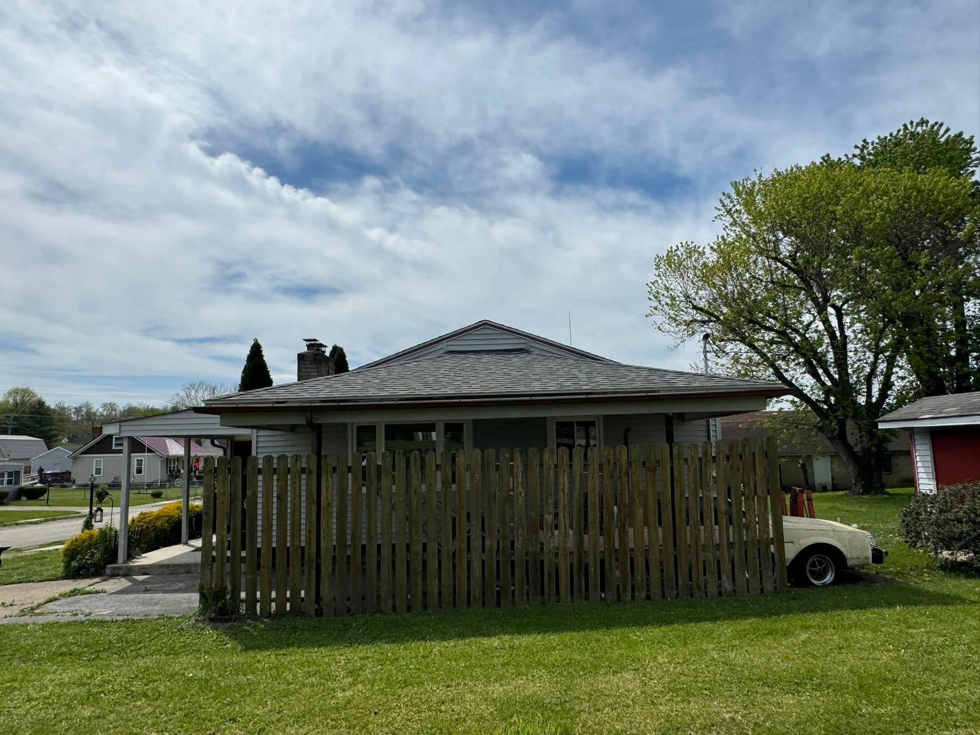 A white car is parked in front of a house with a wooden fence.