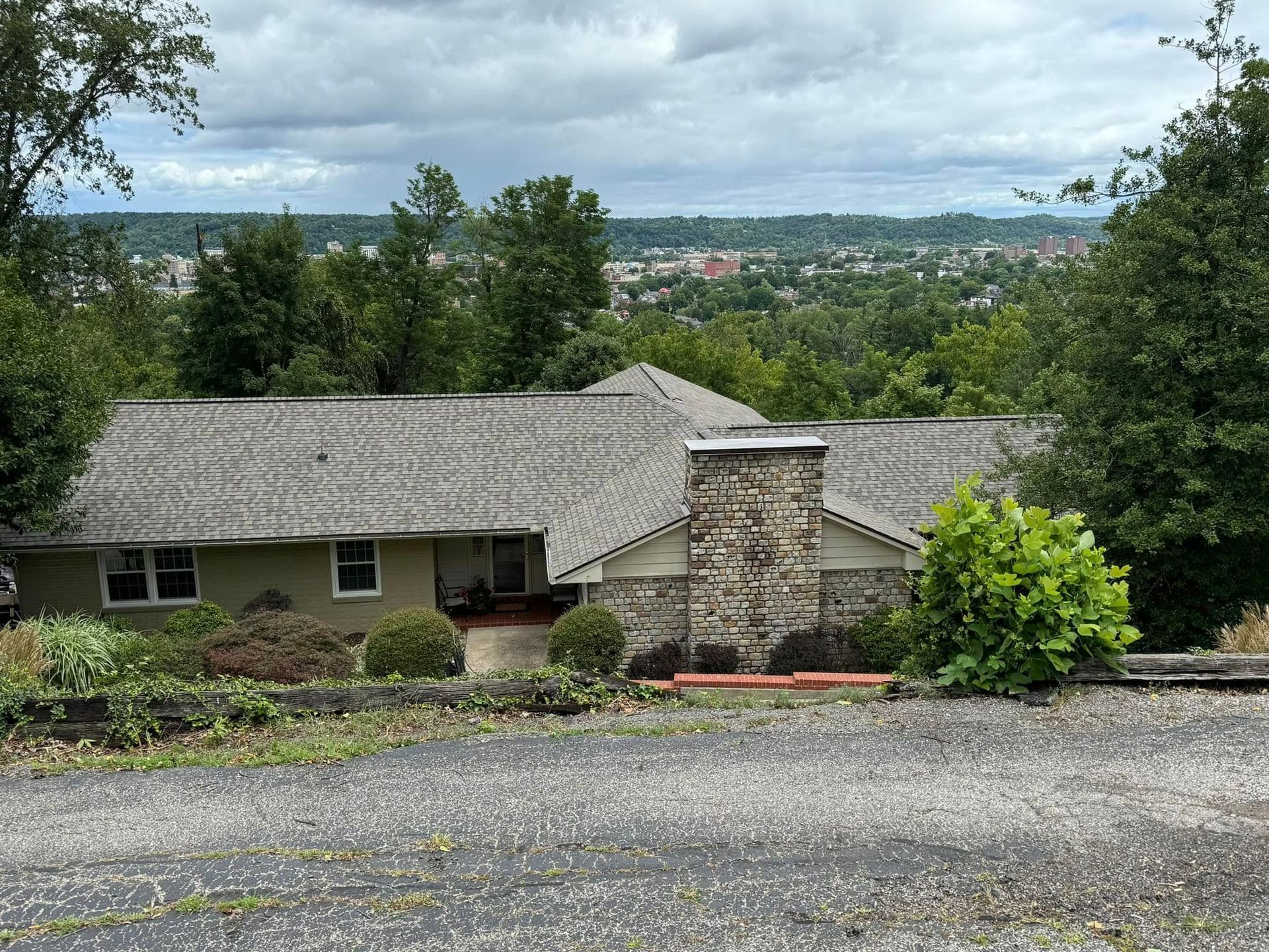 A house with a gray roof is surrounded by trees and a gravel driveway.