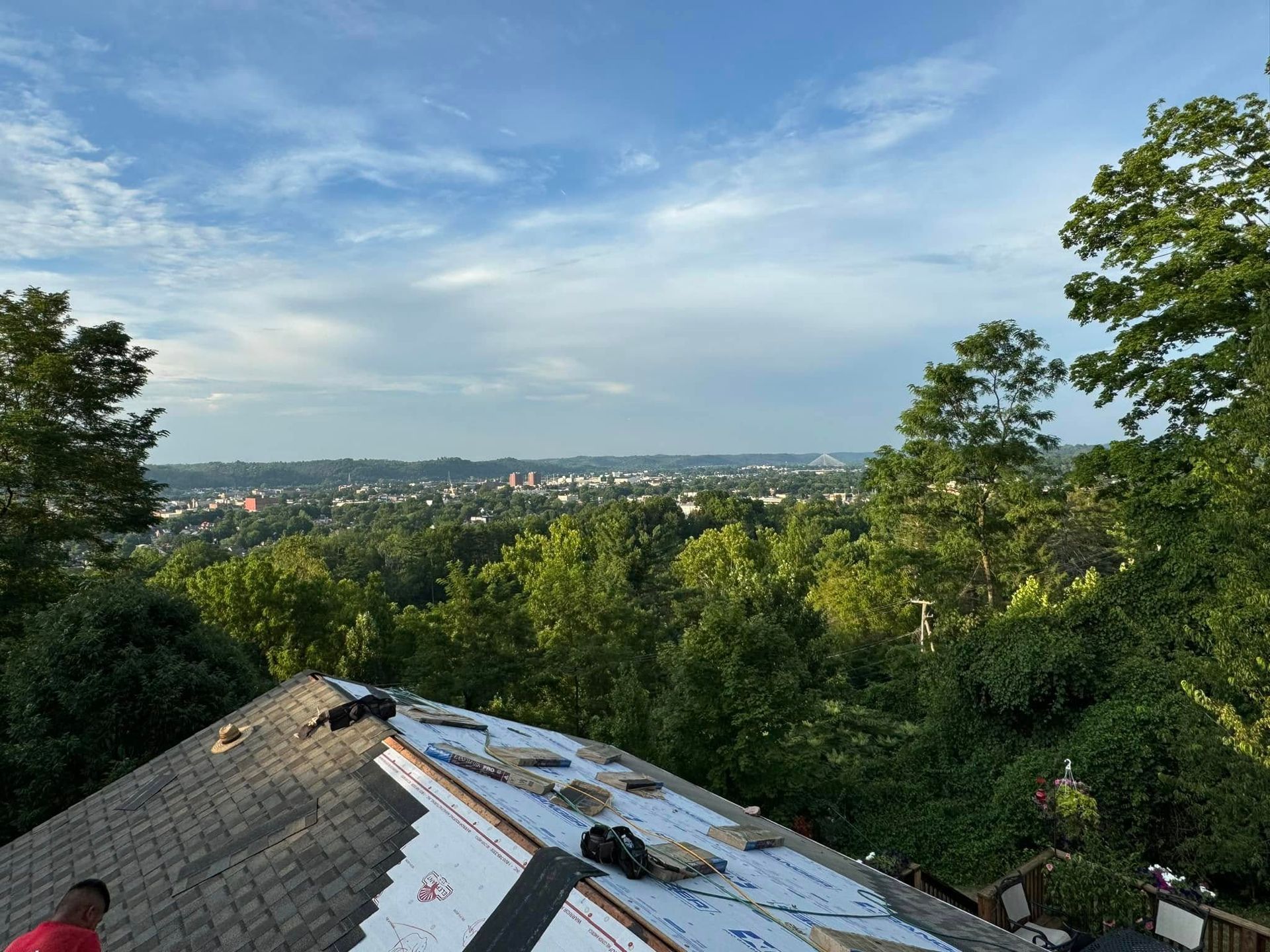 A man is working on the roof of a house with a view of a city.