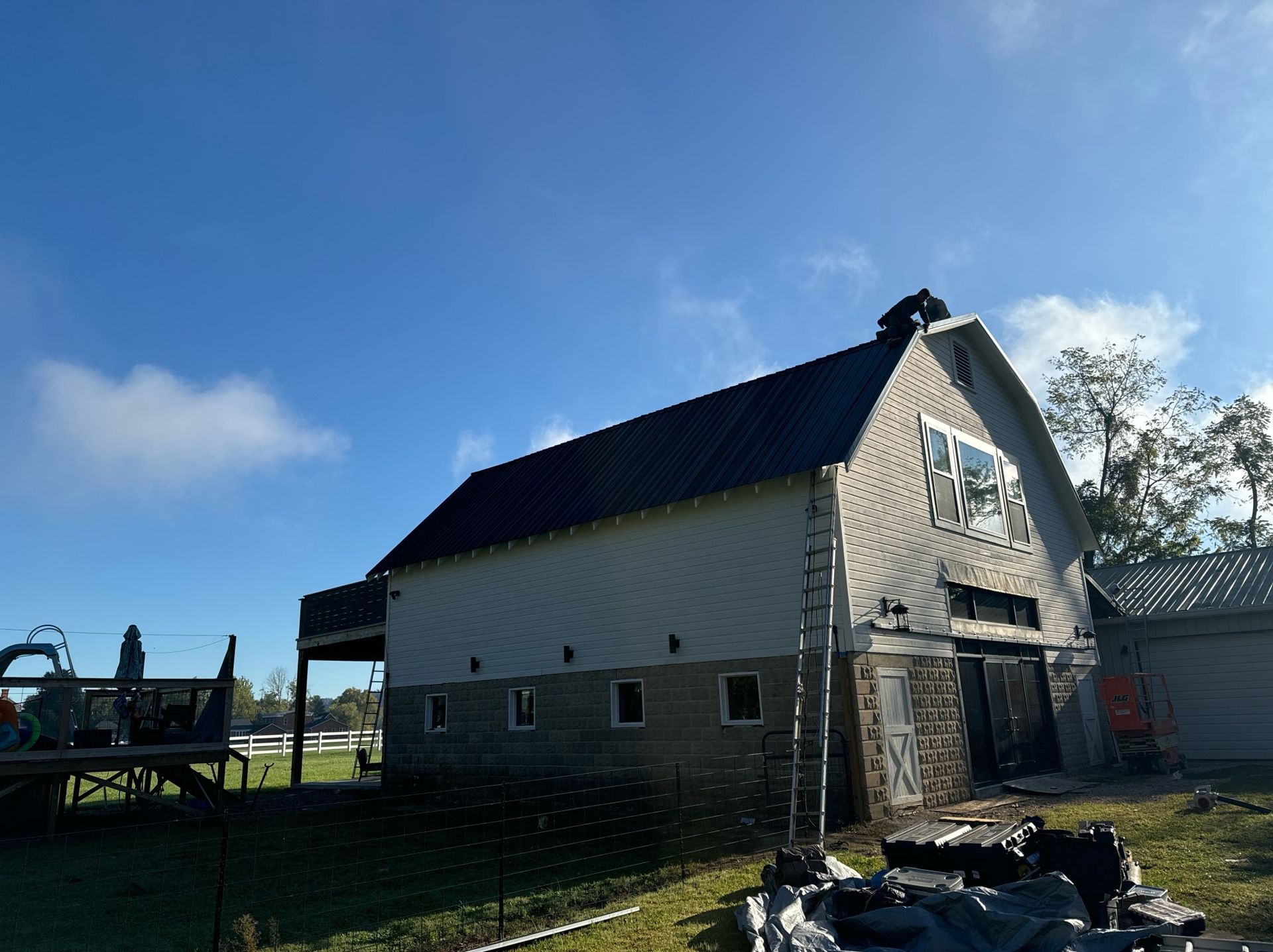 A large white barn with a black roof is sitting in the middle of a grassy field.
