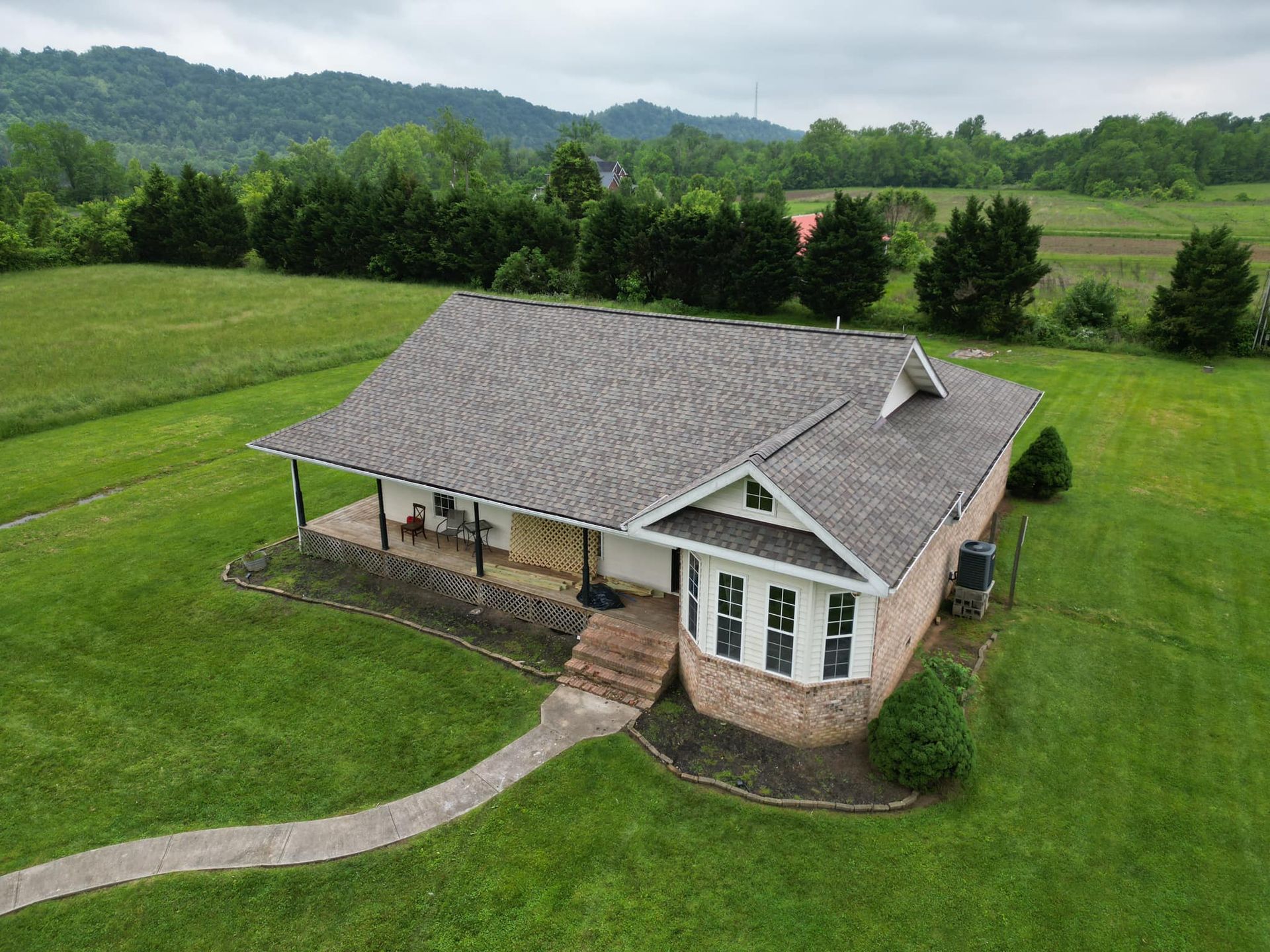 An aerial view of a house in the middle of a grassy field with mountains in the background.