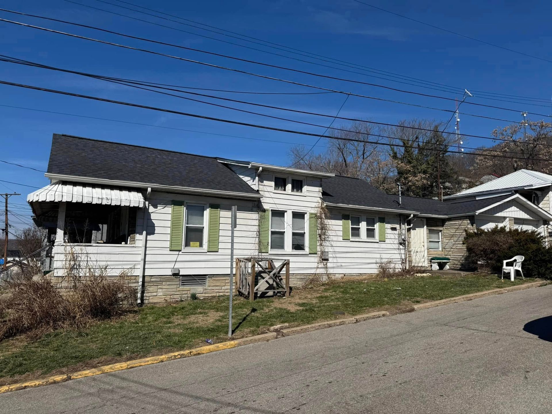 A white house with green shutters is sitting on the side of a road.