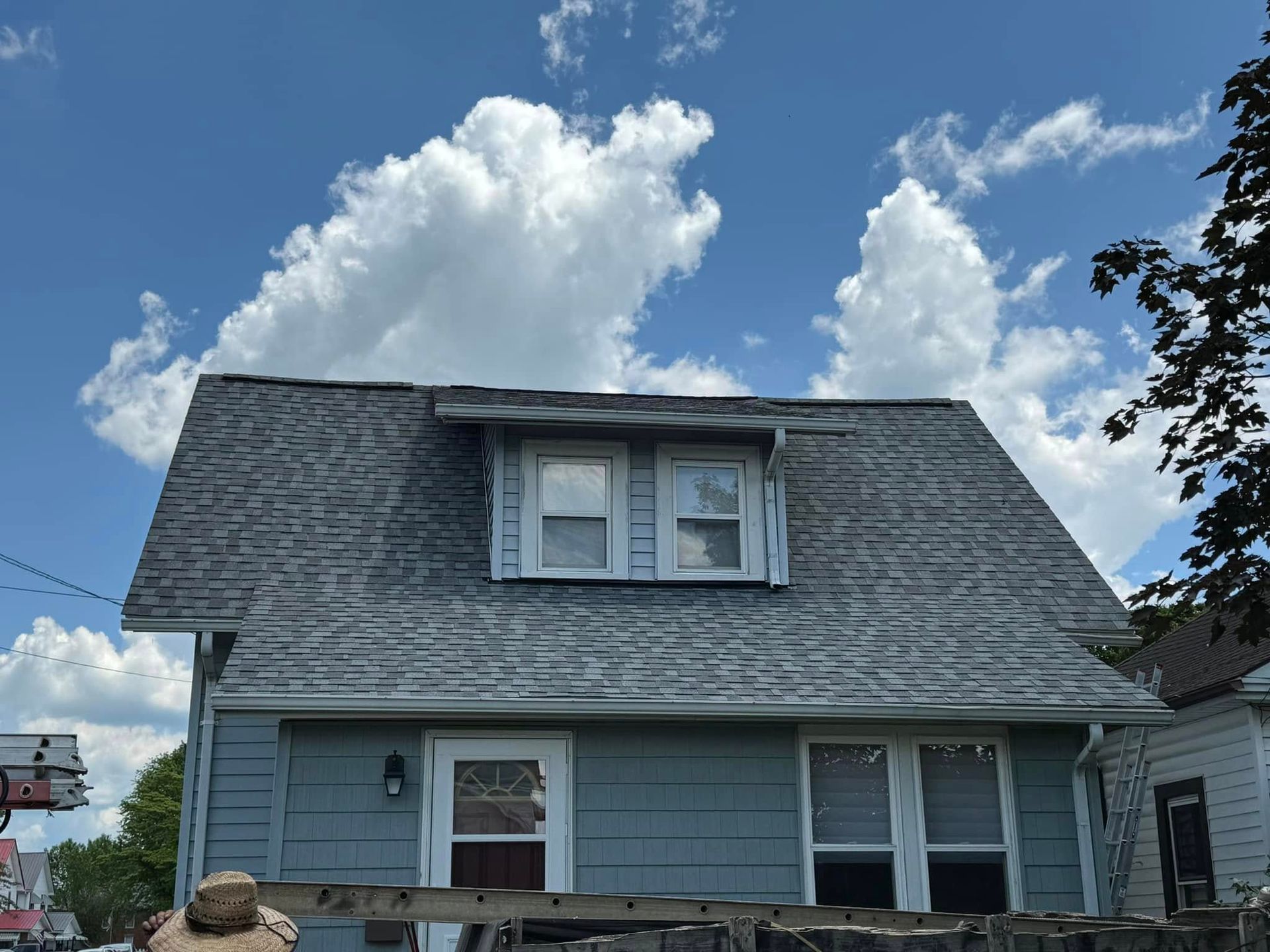A blue house with a gray roof and a blue sky with clouds in the background.
