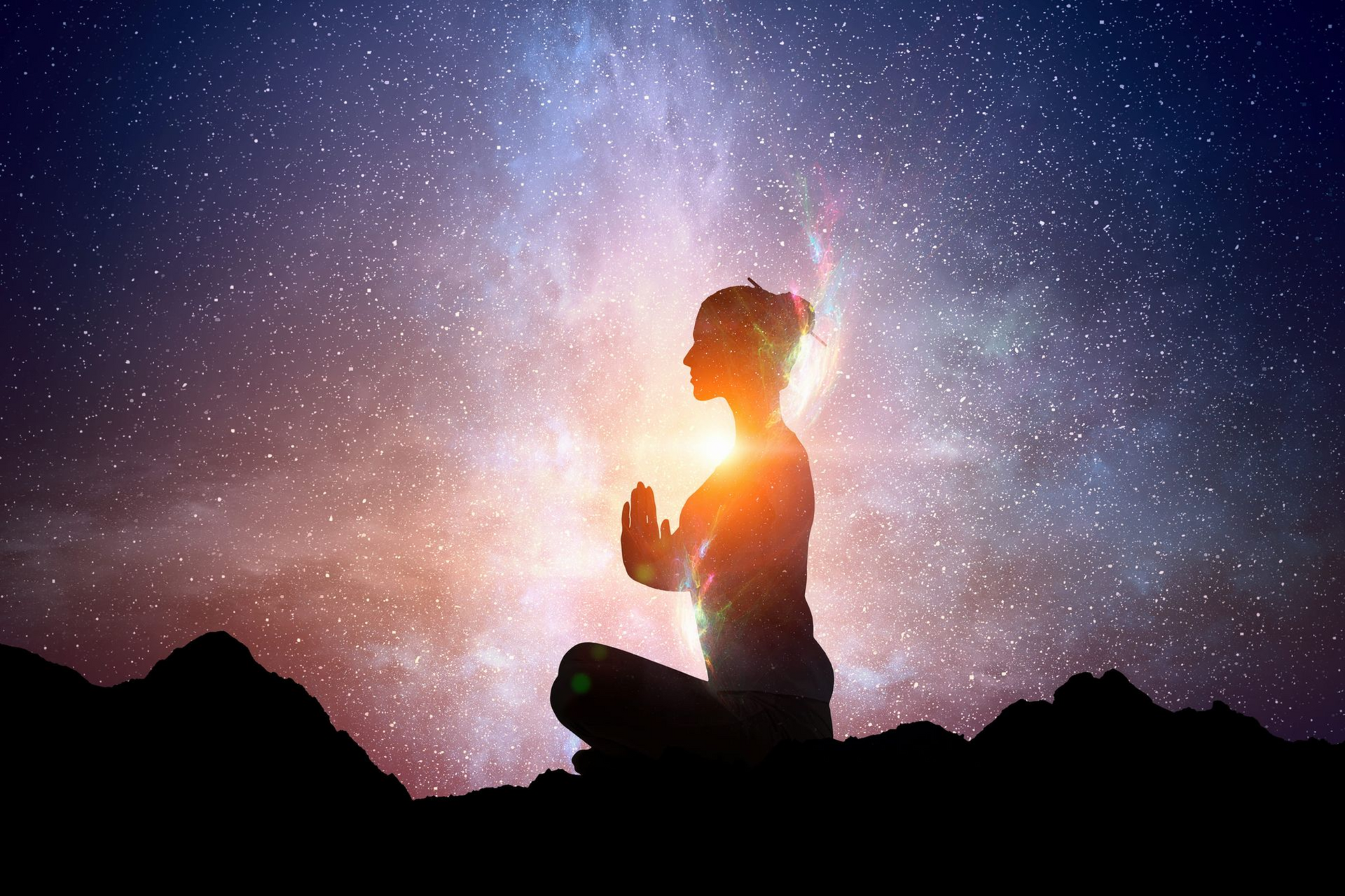 Person meditating in silhouette against a glowing starry sky at sunset