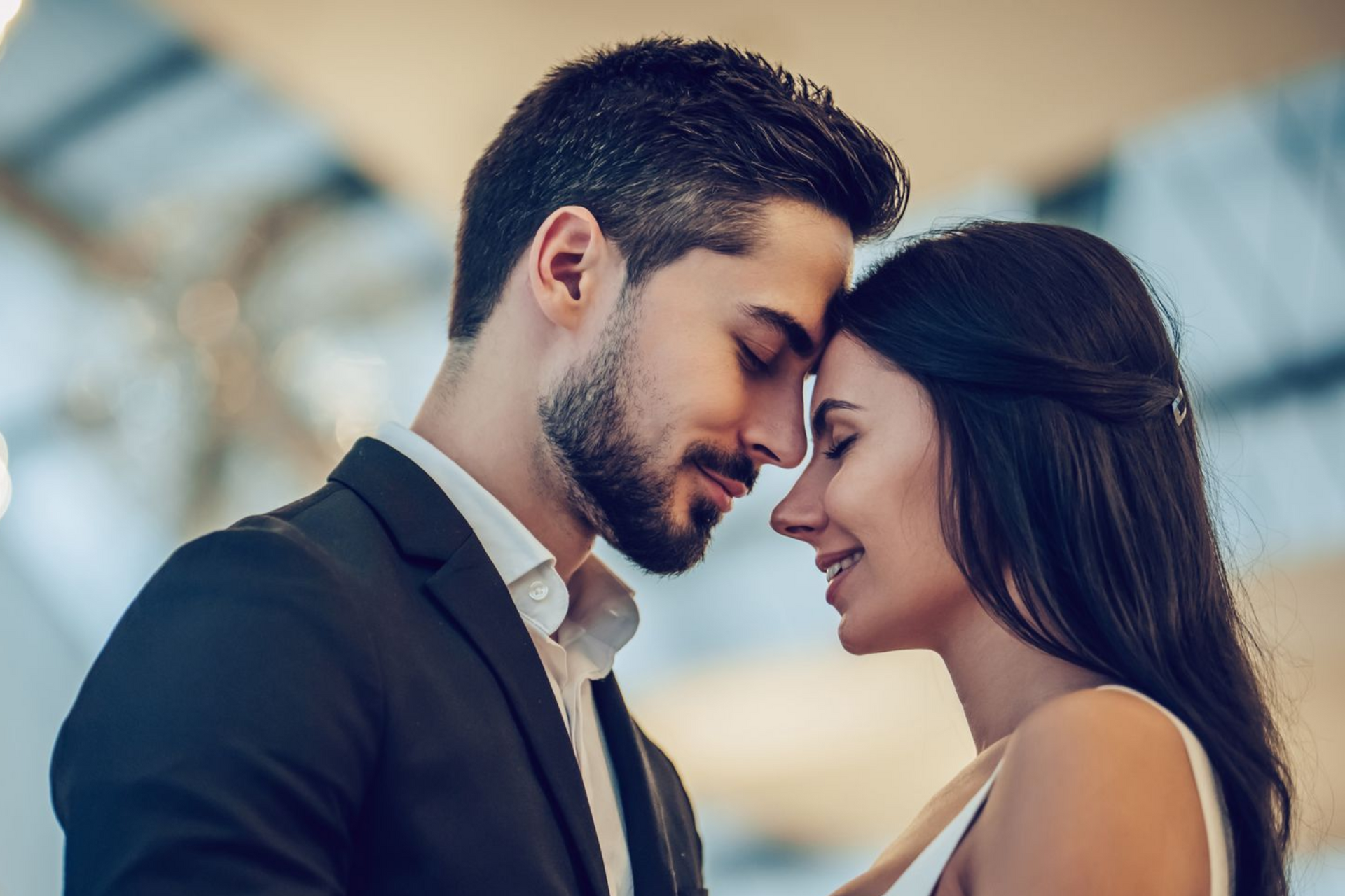 Two people leaning forehead to forehead, smiling in a softly lit indoor setting