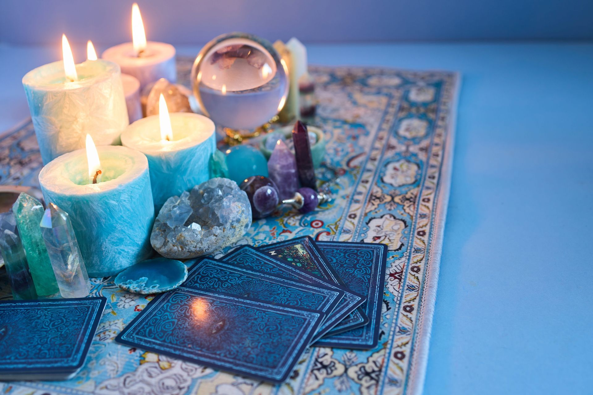 Lit candles, crystals, and blue tarot cards on a patterned cloth