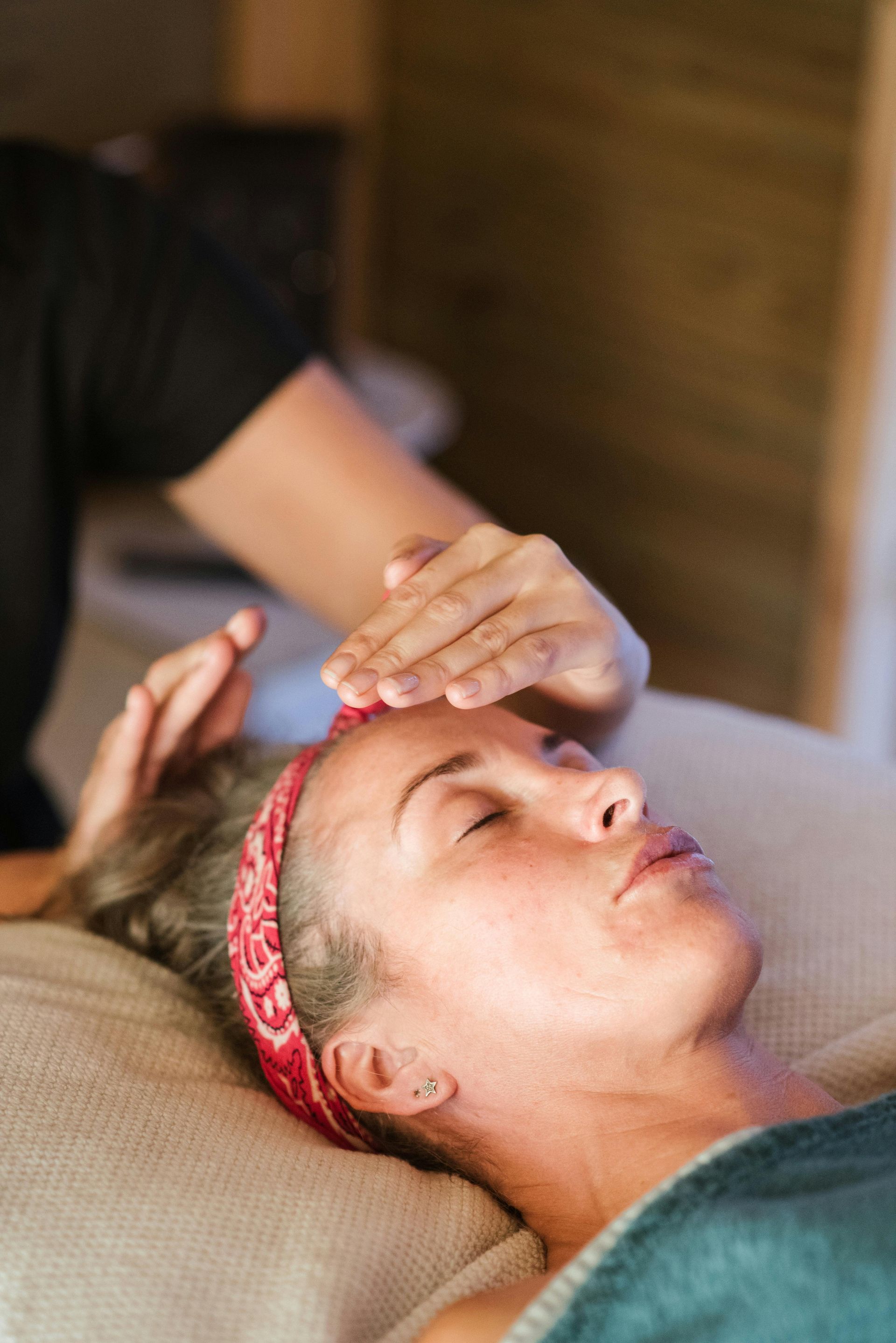 Woman receiving a forehead massage while lying on a couch with a red headband