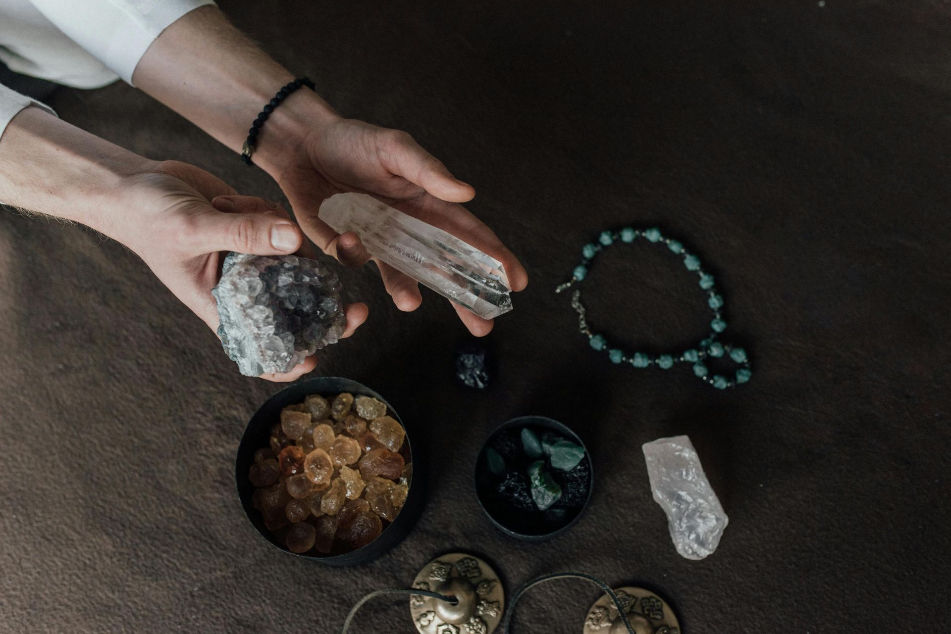 Hands arranging crystals and beads on a dark tabletop with bowls of stones and candles