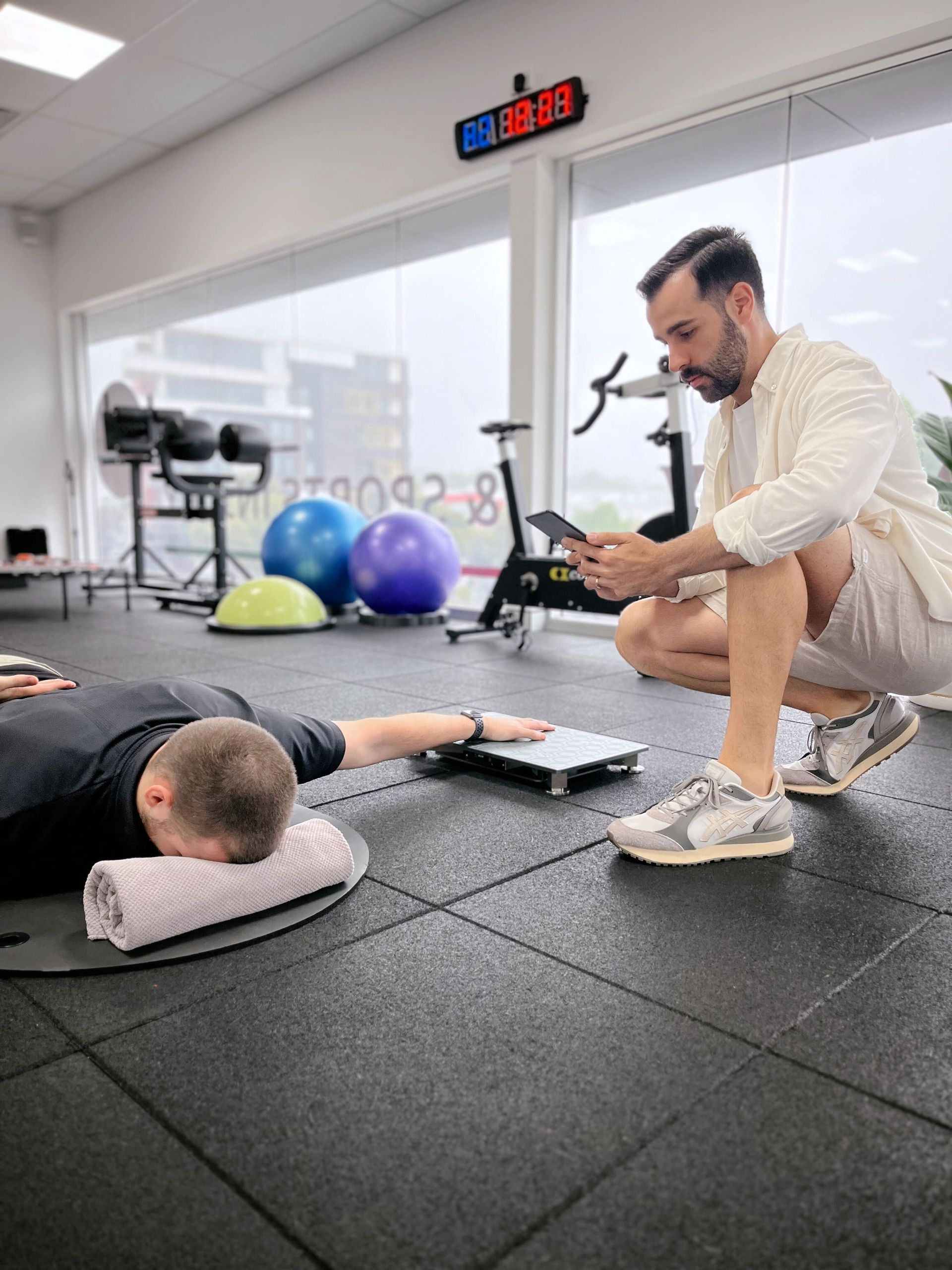 A man is kneeling next to a man laying on the floor in a gym.