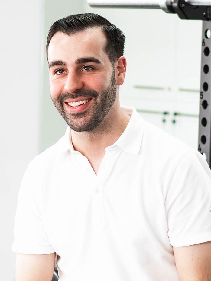 A man with a beard is wearing a white polo shirt and smiling.