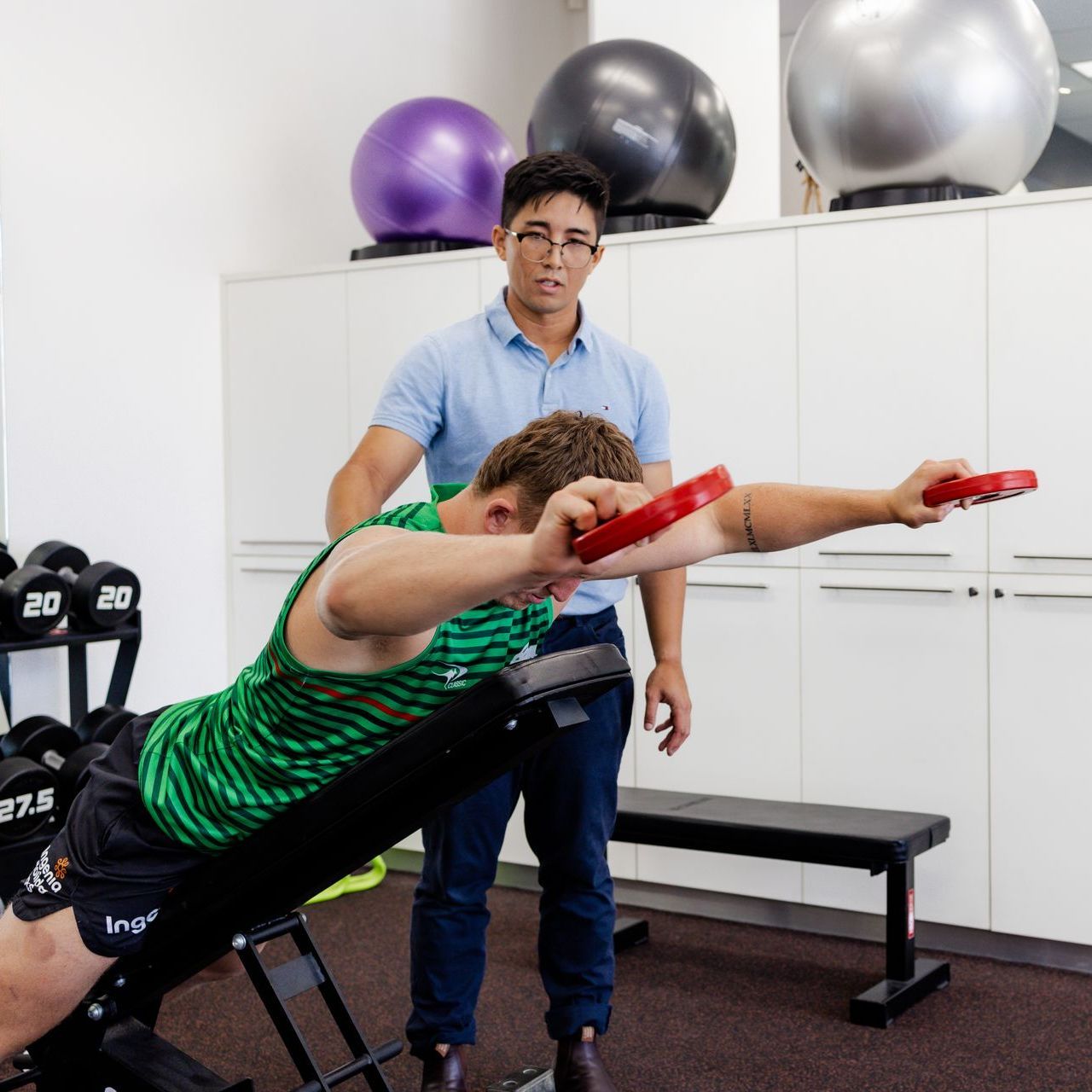 Man on incline bench doing exercise with instructor in a rehab setting.