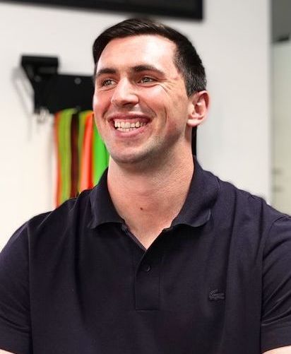 A man in a black polo shirt is smiling.