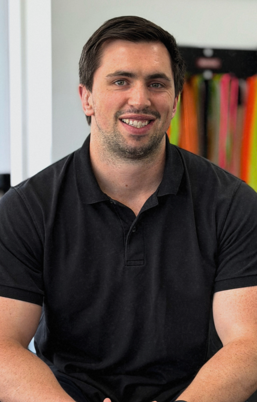 A man in a black polo shirt is smiling.