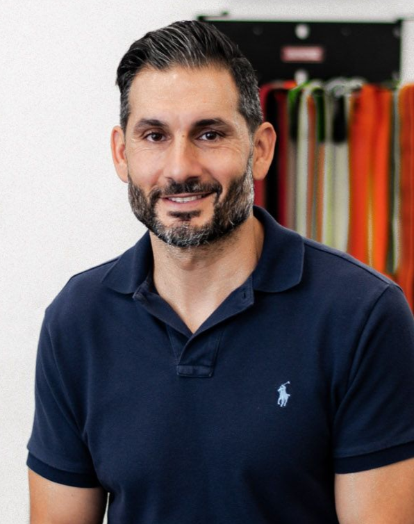 Man in blue polo shirt smiling, background with colorful fabric samples.