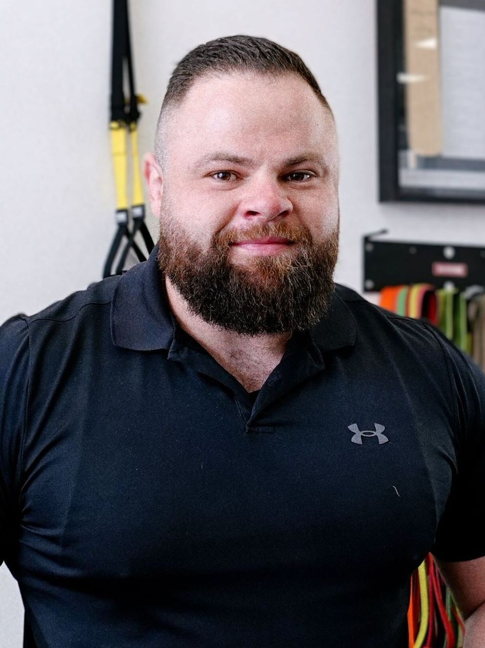 Man with beard wearing black shirt smiles in a therapy setting.