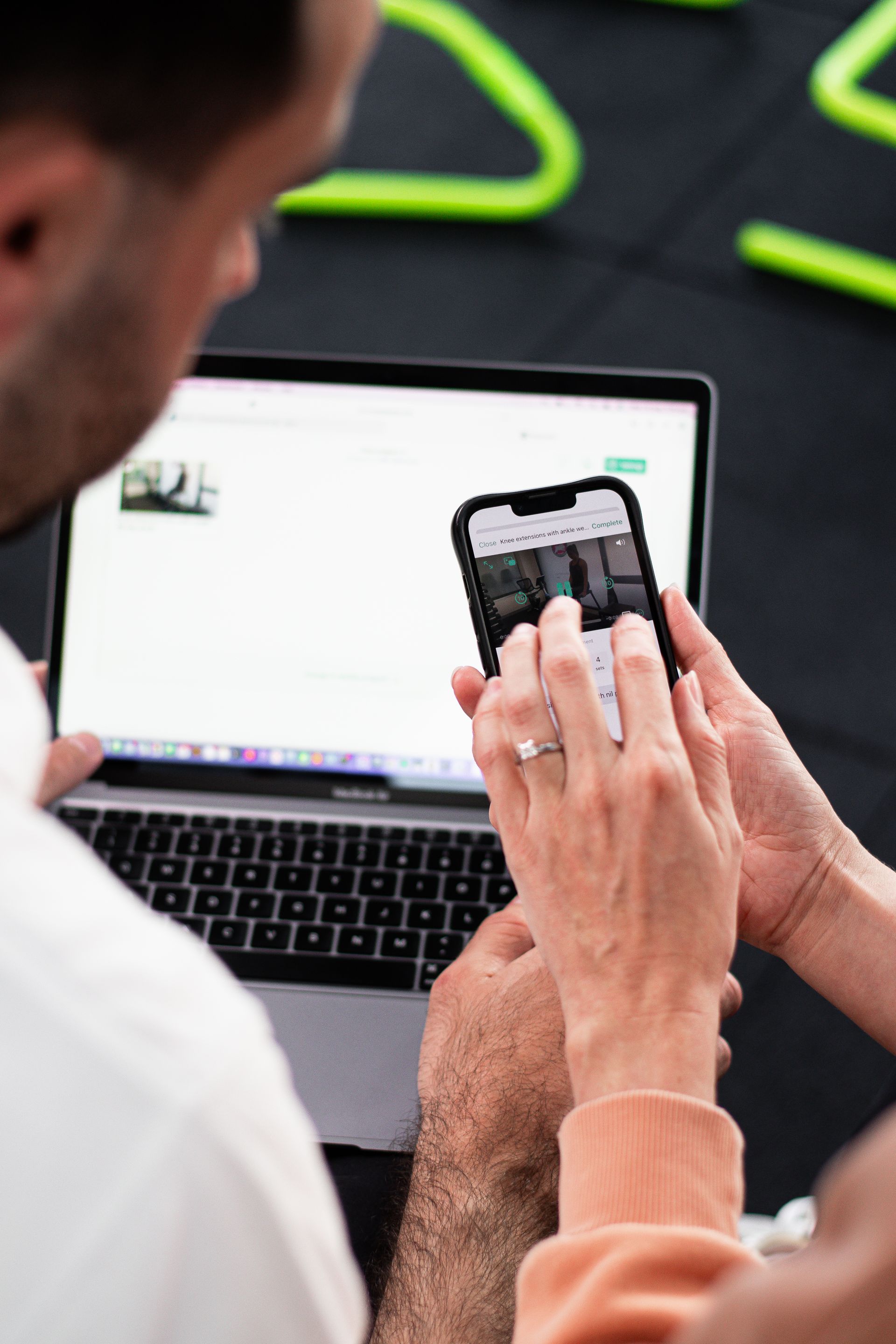 Person looking at laptop and phone. One hand touching the phone screen, the other on the laptop keyboard.