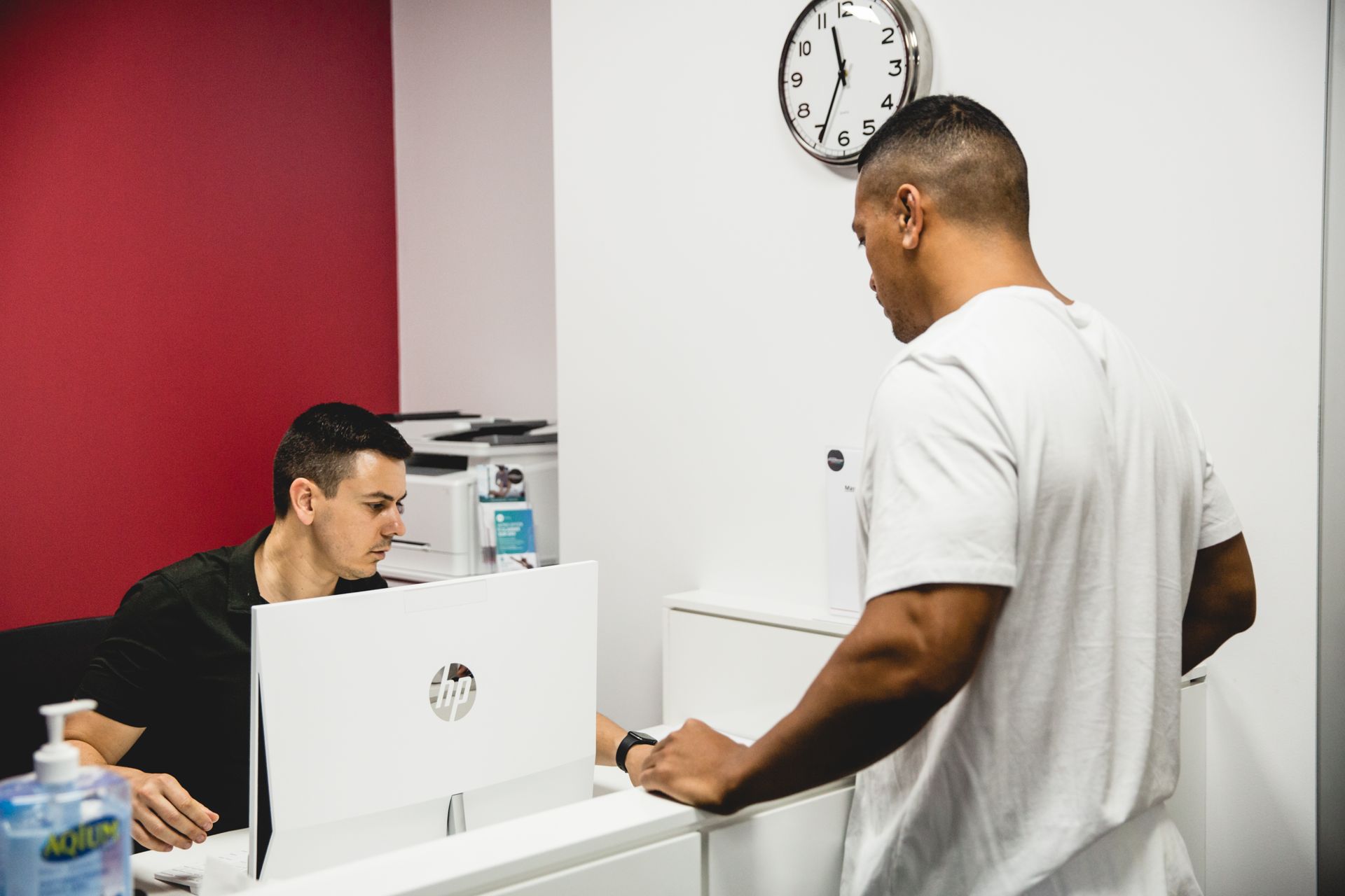A man is standing in front of a computer talking to another man.