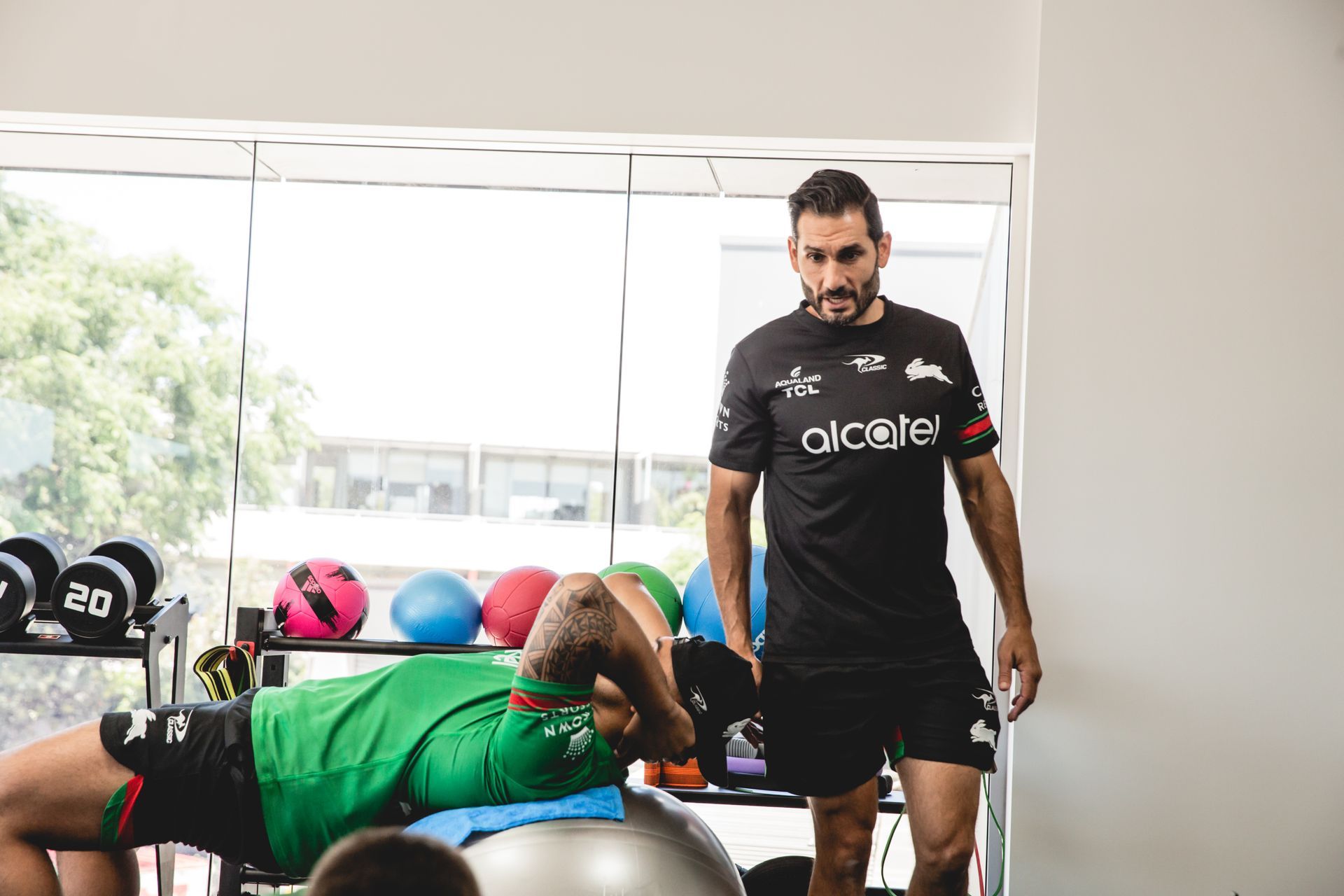 A man is standing next to a man doing push ups in a gym.