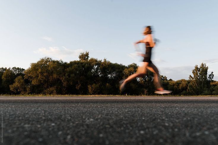 Blurred image of a person running on asphalt with trees in the background.