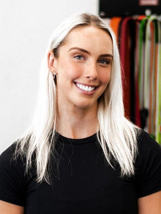 Blonde woman smiling, wearing a black shirt, in front of colorful exercise bands.