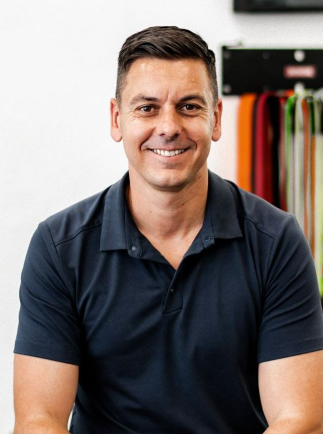 Man wearing a navy polo shirt smiles, posing indoors near fabric swatches.