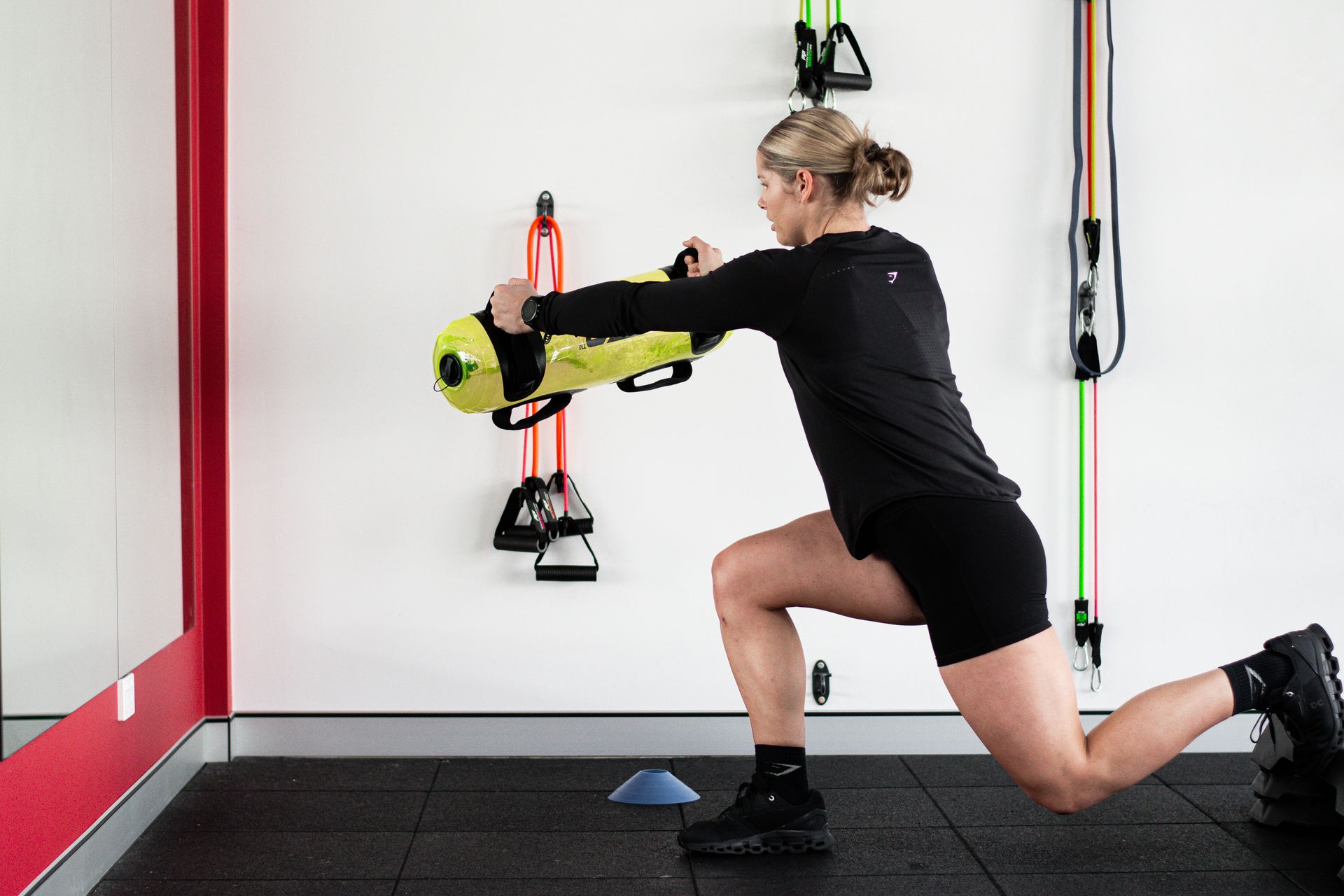 A woman is doing lunges with a yellow bag in a gym.