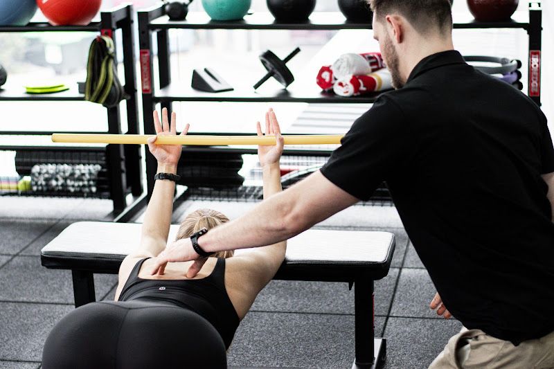 A man is helping a woman do exercises on a bench in a gym.