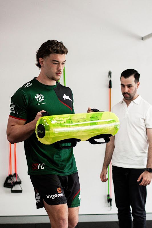 A man in a green shirt is holding a yellow bag while a man in a white shirt stands behind him.