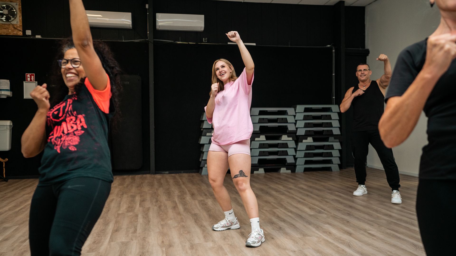Blonde vrouw lacht, dansend in Zumba-kleding. Buiten.