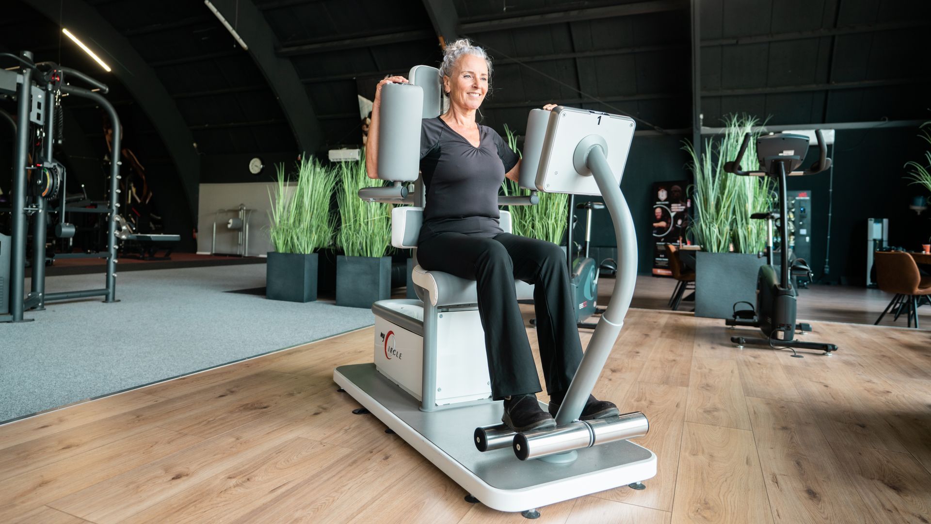 Vrouw in sportkleding zwaait met een kettlebell. Blond haar, geconcentreerde uitdrukking. Sportschoolomgeving.