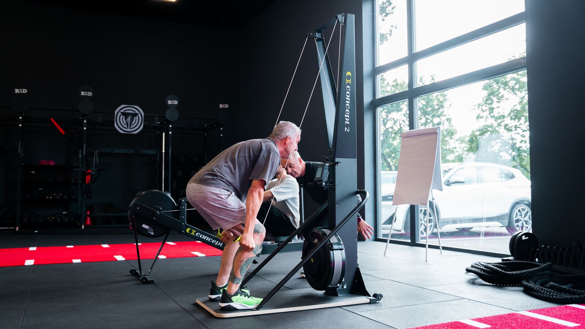 Twee rijen zwarte kettlebells op de vloer van een sportschool, naast een rood rek.