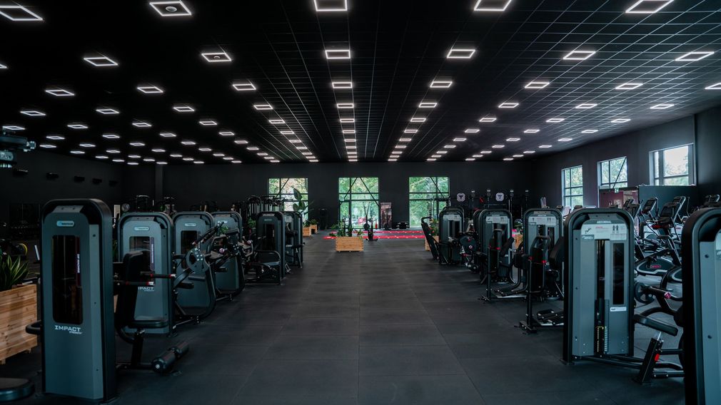 Een man rent op een loopband in een sportschool, naast twee anderen, met een groot raam op de achtergrond.