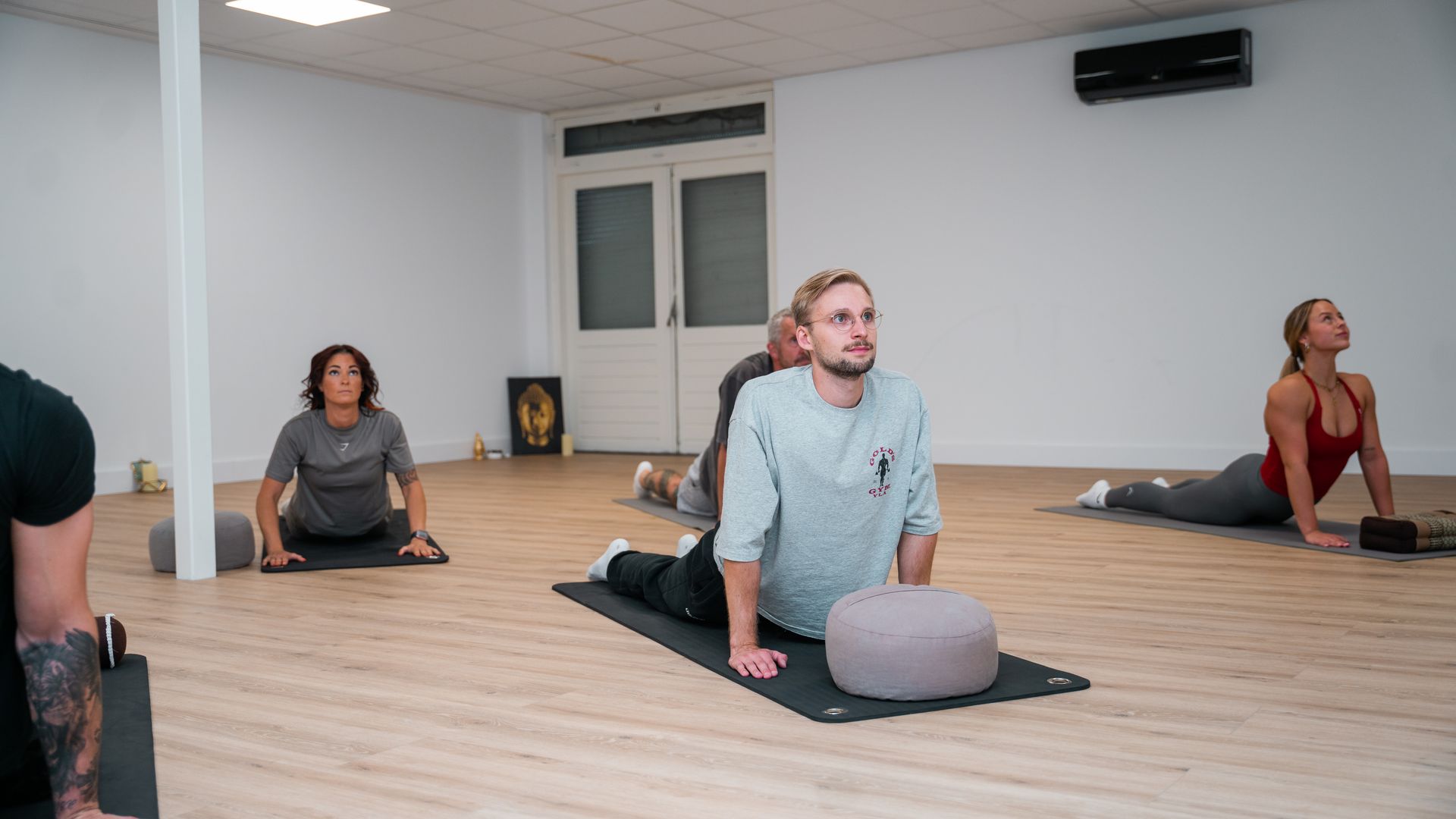 Mensen sporten binnen, met hoge knieën en rode matten op de vloer.