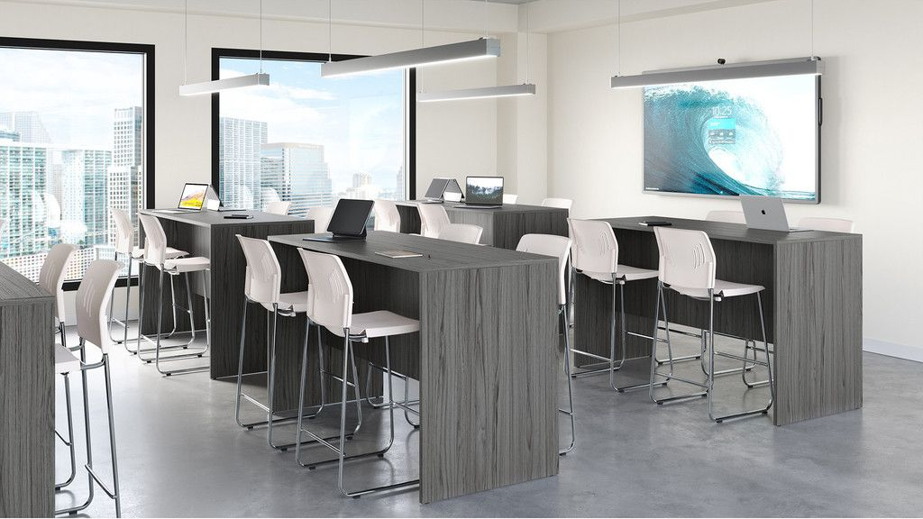 Modern classroom with gray high tables, white stools, and a large screen.